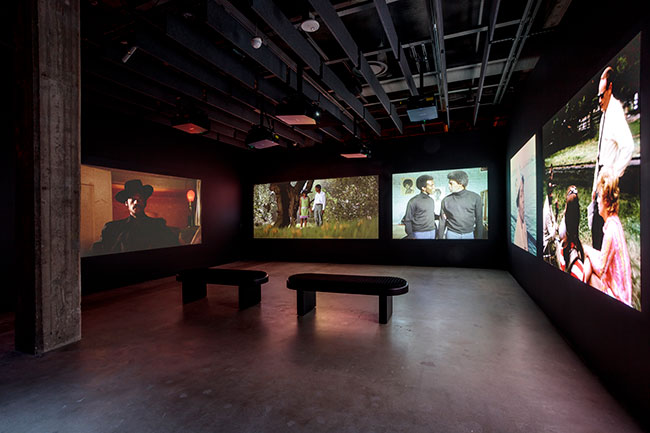 Film images projected from projectors hung from the ceiling onto walls in a dark room