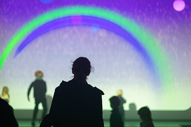 A person is backlit in front of a projected image of a rainbow