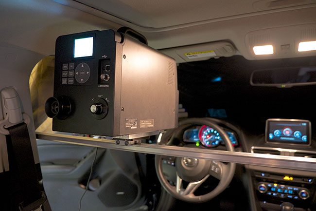 A black electronic box is mounted at eye-level in the driver’s seat of a car.
