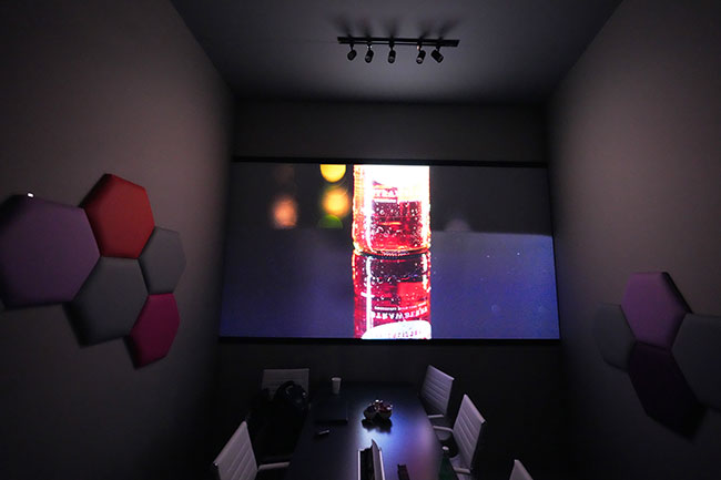 Image of a colorful bottle is projected onto a screen in a meeting room.