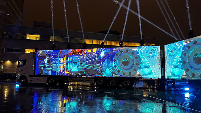 A truck is projection mapped with images of gears in shades of blue.