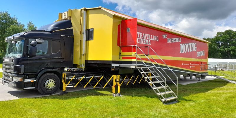 A transport truck with a red trailer with stairs up to a door in the side of the trailer.