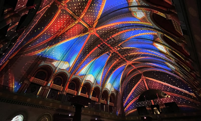 An ornate barrel-shaped ceiling is projection mapped with vivid colors.