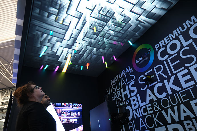 Two people looking up at a projection on a small screen on the ceiling of a small black room.  